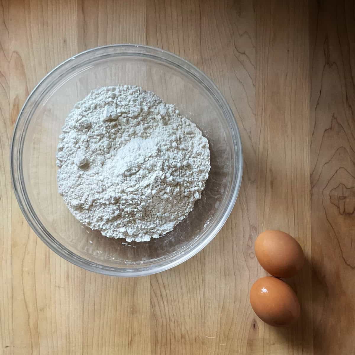 Ingredients to make egg pasta dough on a wooden board.