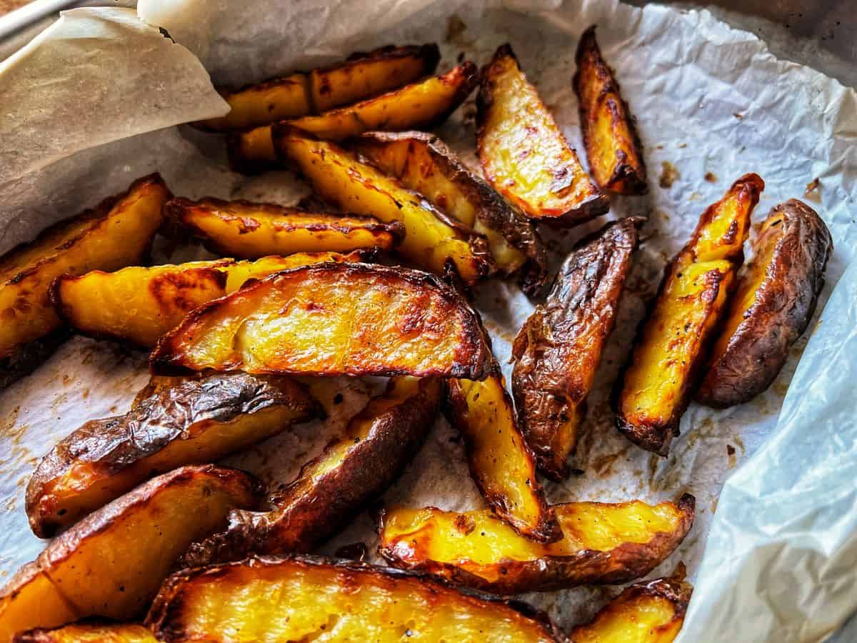 Simple, golden baked potato wedges cooling on parchment paper after roasting.