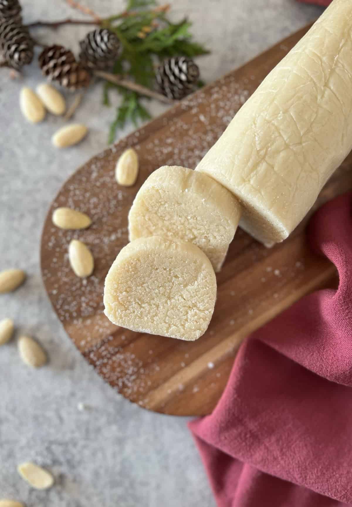 An overhead photo of an almond paste log sliced into a few even rounds on a wooden cutting board.