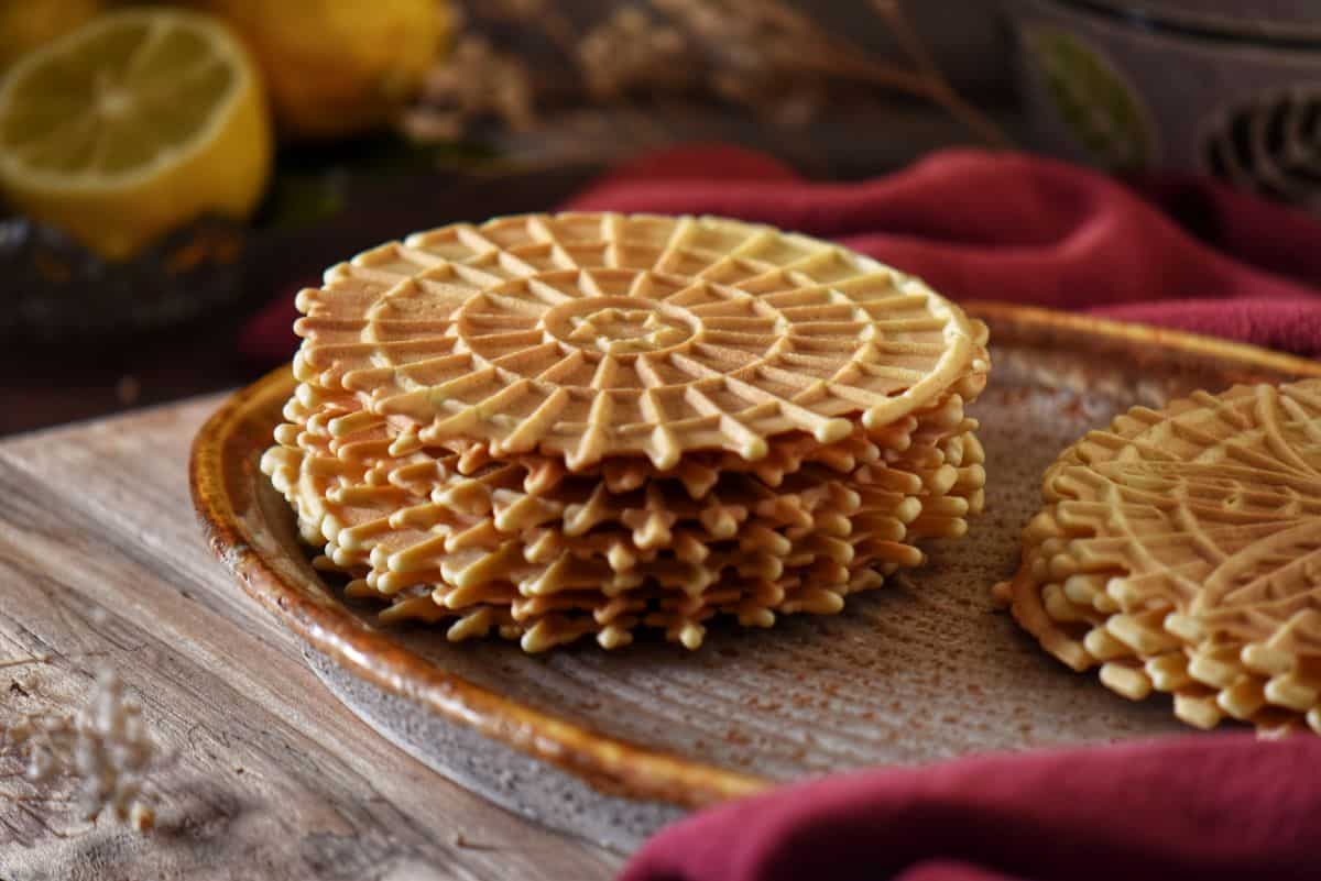 A stack of crisp lemon pizzelle cookies with fresh lemons in the background.