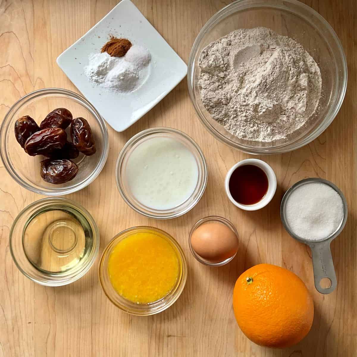 Ingredients for healthy orange muffins including whole orange, dates, whole wheat flour, and baking staples.