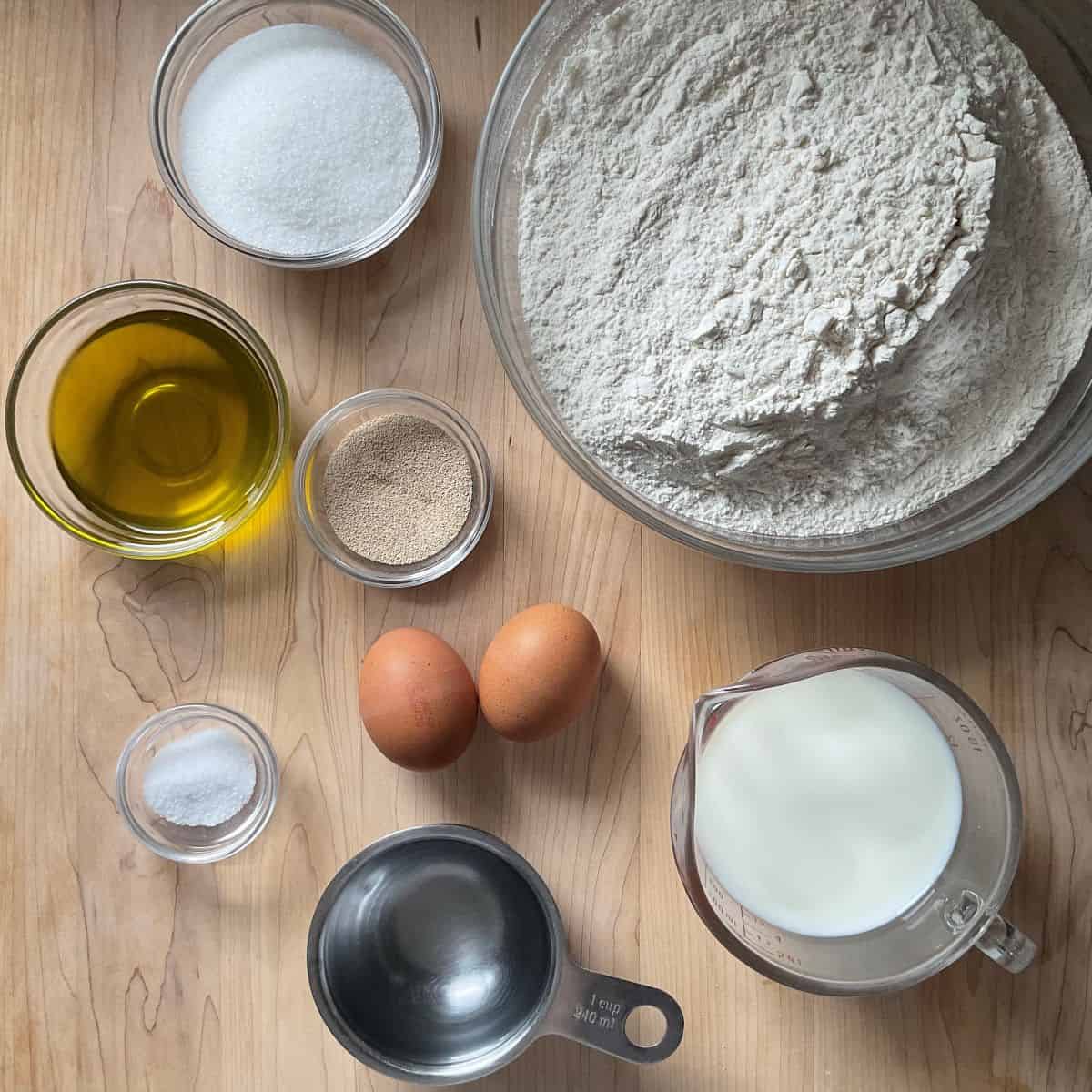 Ingredients to make soft dinner rolls with olive oil on a wooden board.