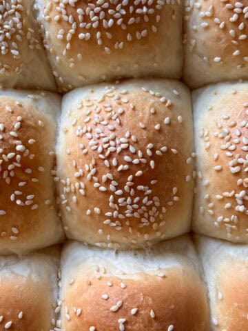 Overhead view, of freshly baked, golden soft dinner rolls garnished with sesame seeds.