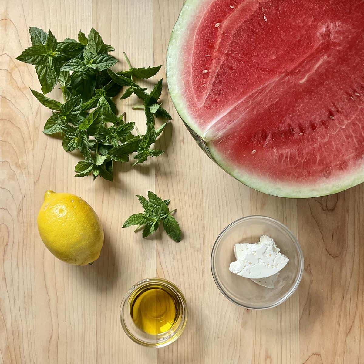 Ingredients for watermelon feta mint salad including seedless watermelon, block feta cheese, fresh mint leaves, lemon and olive oil