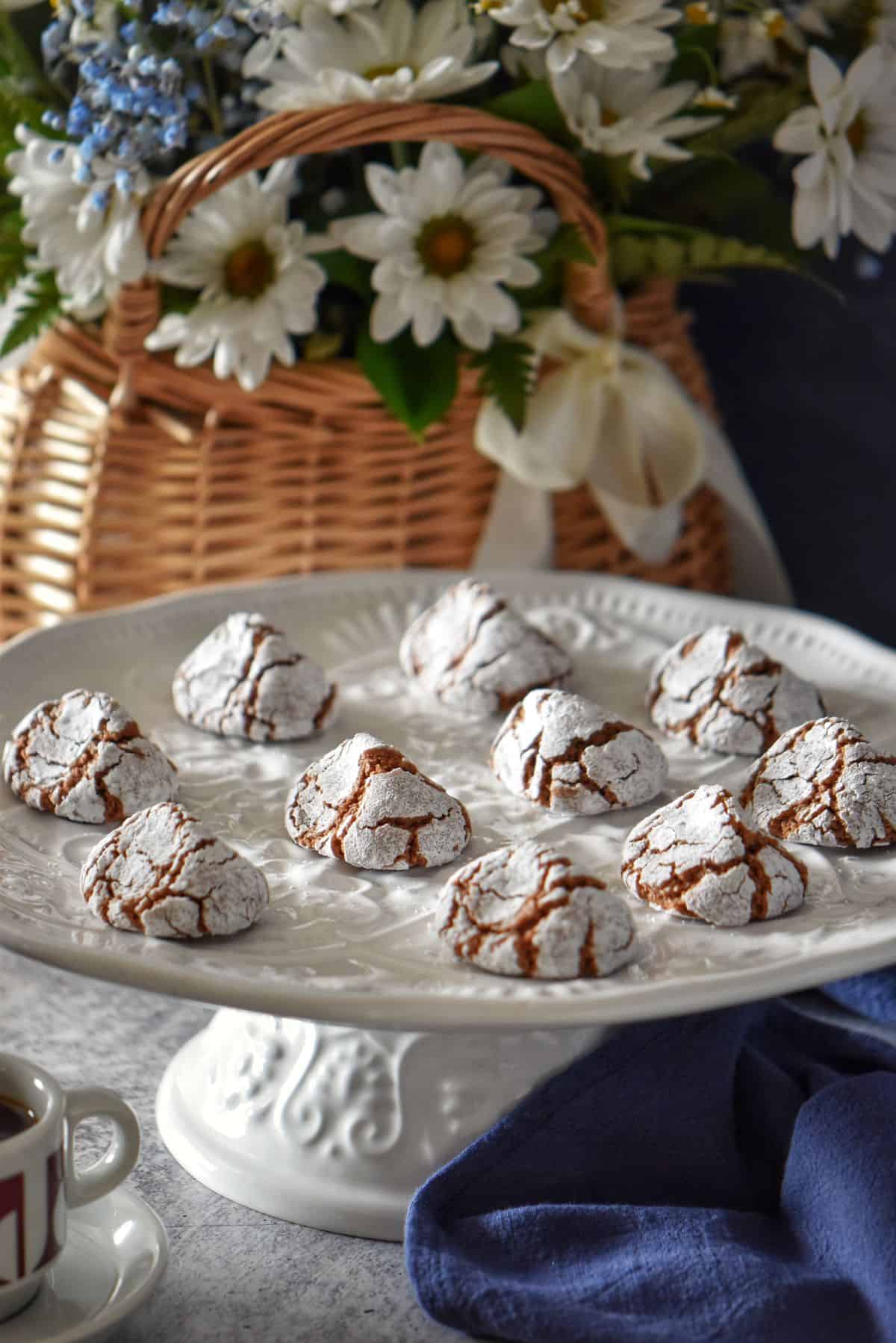 Chocolate amaretti cookies on a white platter next to a cup of espresso